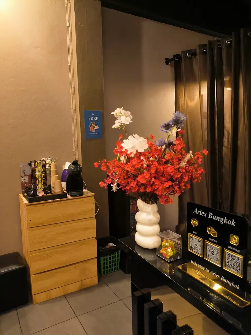 Coffee corner with a wooden drawer unit, red and white flowers and an Aries Bangkok welcome sign